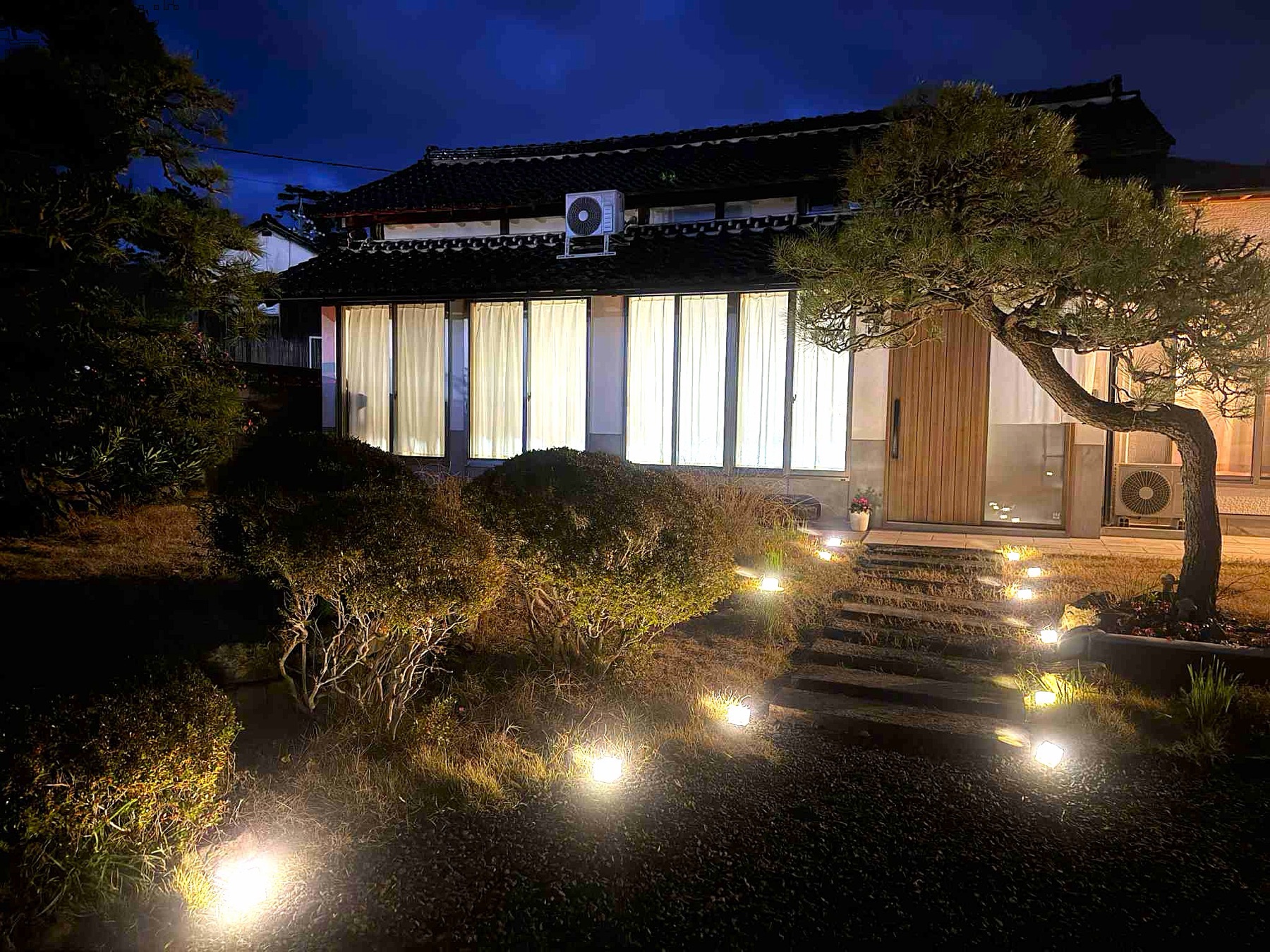 夜、灯りがともる KAMIGOTO HOUSE の外観と松の木